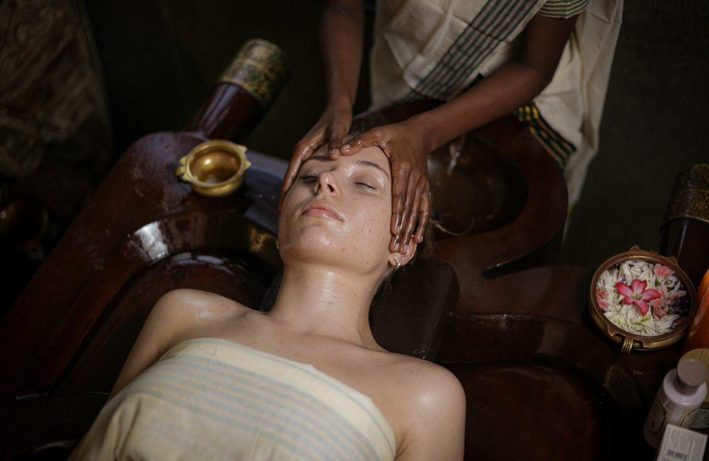 Woman receiving Ayurvedic Shirodhara therapy at a traditional Ayurvedic nature retreat for nervous system relaxation