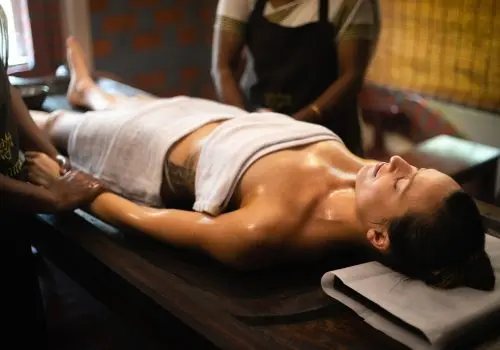 Woman receiving a traditional Ayurvedic oil massage (Abhyanga) on a wooden massage table at a wellness retreat