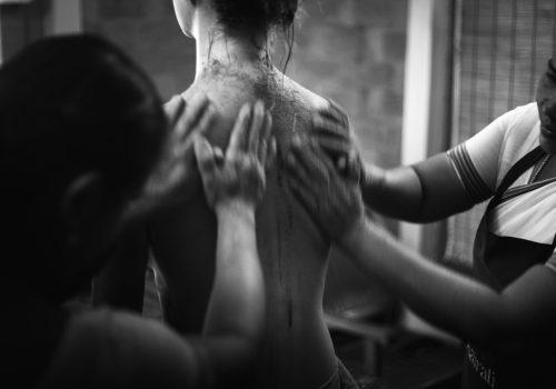 Two therapists apply a body treatment to a woman’s back in a wellness setting.