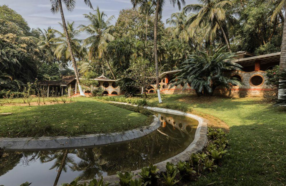 Serene landscape of Kairali Ayurvedic Healing Village in Kerala featuring traditional cottages, palm trees, and tranquil water stream for Ayurveda retreat India
