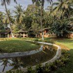 Serene landscape of Kairali Ayurvedic Healing Village in Kerala featuring traditional cottages, palm trees, and tranquil water stream for Ayurveda retreat India