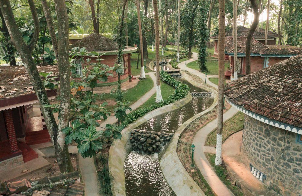 Serene forest-based Ayurvedic healing village in Kerala with traditional cottages, flowing water channels, and lush greenery supporting Panchakarma therapy