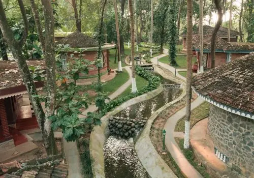 Serene forest-based Ayurvedic healing village in Kerala with traditional cottages, flowing water channels, and lush greenery supporting Panchakarma therapy