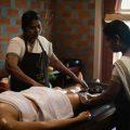 A woman receiving a traditional Ayurvedic massage from two therapists at Kairali spa, lying on a wooden massage table