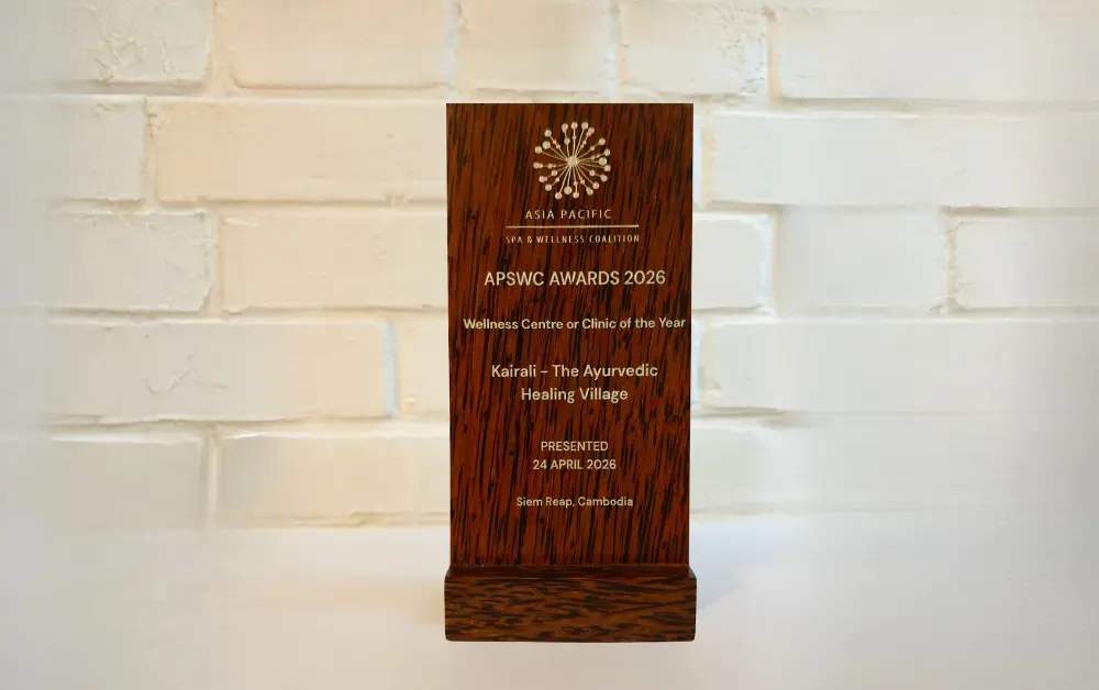 Wooden award plaque from the Asia Pacific Spa & Wellness Coalition, engraved with "APSWC Awards 2026 – Wellness Centre or Clinic of the Year – Kairali – The Ayurvedic Healing Village – Presented 24 April 2026, Siem Reap, Cambodia.