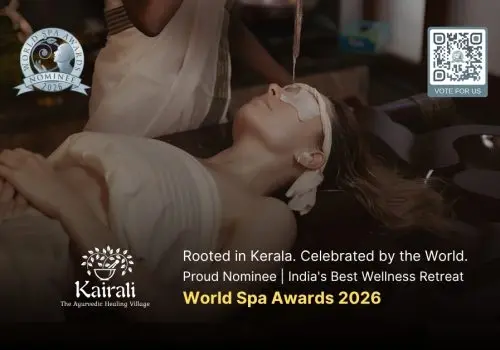A therapist performs Shirodhara, an Ayurvedic treatment, pouring a stream of warm oil onto the forehead of a woman lying peacefully on a treatment table, with eye pads and ear coverings in place.