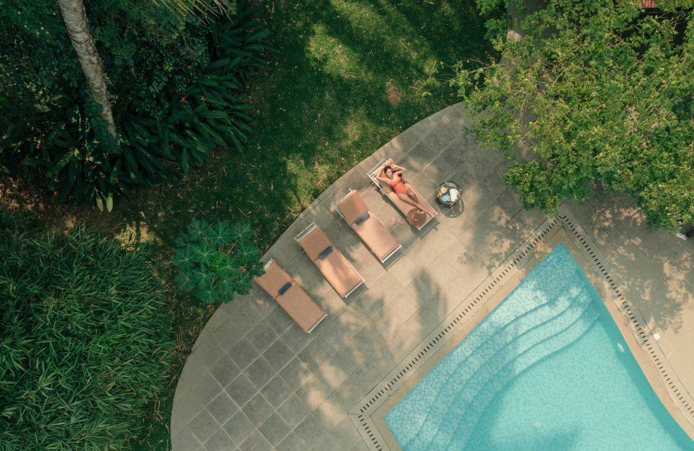 Woman relaxing beside a swimming pool at a luxury Ayurvedic wellness retreat in Kerala surrounded by lush greenery during summer