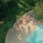 Woman relaxing beside a swimming pool at a luxury Ayurvedic wellness retreat in Kerala surrounded by lush greenery during summer