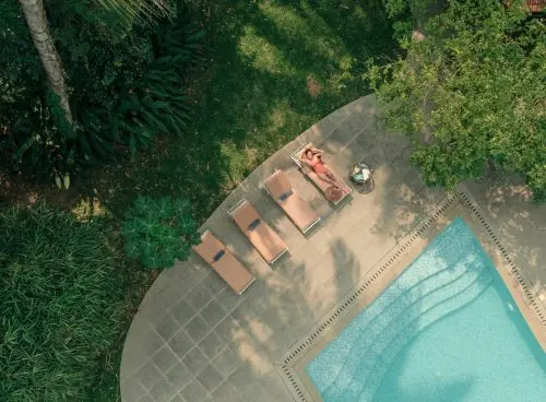 Woman relaxing beside a swimming pool at a luxury Ayurvedic wellness retreat in Kerala surrounded by lush greenery during summer