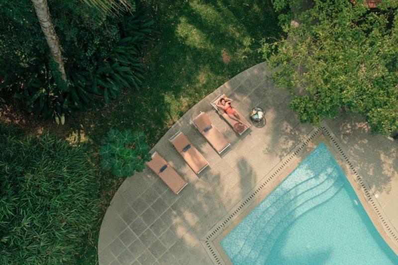 Woman relaxing beside a swimming pool at a luxury Ayurvedic wellness retreat in Kerala surrounded by lush greenery during summer