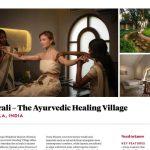 Two Ayurvedic therapists in traditional white sarees performing a synchronised arm massage treatment on a female guest at Kairali – The Ayurvedic Healing Village in Kerala, India, inside a warmly lit treatment room with an arched window.