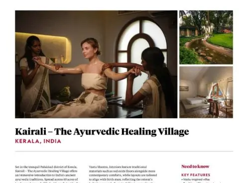 Two Ayurvedic therapists in traditional white sarees performing a synchronised arm massage treatment on a female guest at Kairali – The Ayurvedic Healing Village in Kerala, India, inside a warmly lit treatment room with an arched window.