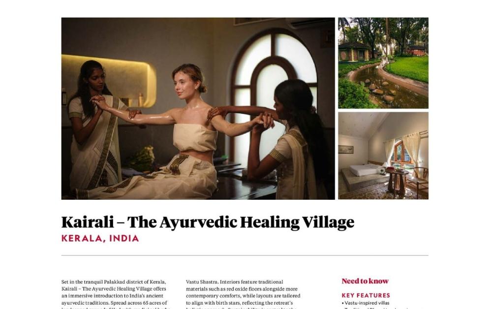 Two Ayurvedic therapists in traditional white sarees performing a synchronised arm massage treatment on a female guest at Kairali – The Ayurvedic Healing Village in Kerala, India, inside a warmly lit treatment room with an arched window.