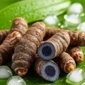 Fresh black turmeric roots displayed on green leaves with ice cubes, highlighting Ayurvedic summer wellness and natural cooling benefits.