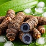 Fresh black turmeric roots displayed on green leaves with ice cubes, highlighting Ayurvedic summer wellness and natural cooling benefits.
