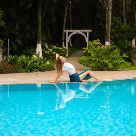 Woman relaxing beside a swimming pool surrounded by tropical greenery at Kairali – The Ayurvedic Healing Village in Kerala, India.