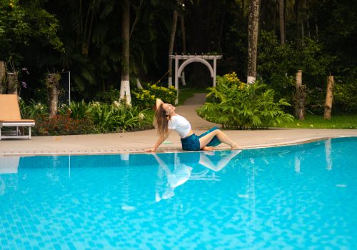 Woman relaxing beside a swimming pool surrounded by tropical greenery at Kairali – The Ayurvedic Healing Village in Kerala, India.