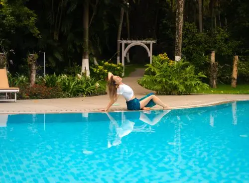 Woman relaxing beside a swimming pool surrounded by tropical greenery at Kairali – The Ayurvedic Healing Village in Kerala, India.
