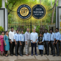 Kairali Ayurvedic Health Resort team posing in front of the resort's entrance gate, with overlaid Haute Grandeur Global Awards 2026 Winner Hotel badges.
