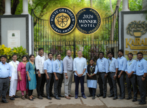 Kairali Ayurvedic Health Resort team posing in front of the resort's entrance gate, with overlaid Haute Grandeur Global Awards 2026 Winner Hotel badges.