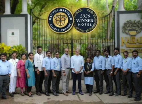 Kairali Ayurvedic Health Resort team posing in front of the resort's entrance gate, with overlaid Haute Grandeur Global Awards 2026 Winner Hotel badges.