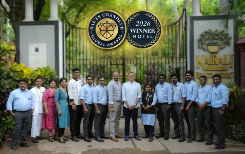 Kairali Ayurvedic Health Resort team posing in front of the resort's entrance gate, with overlaid Haute Grandeur Global Awards 2026 Winner Hotel badges.