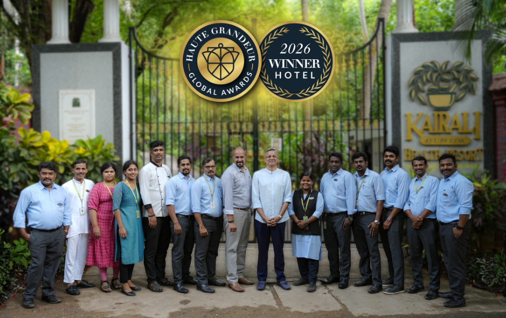 Kairali Ayurvedic Health Resort team posing in front of the resort's entrance gate, with overlaid Haute Grandeur Global Awards 2026 Winner Hotel badges.