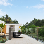 Modern outdoor poolside terrace with a lounge chair, glass railing, and tropical greenery under a blue sky.