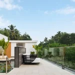 Modern outdoor poolside terrace with a lounge chair, glass railing, and tropical greenery under a blue sky.