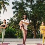 Three people practicing tree pose during a quiet yoga retreat in Goa, surrounded by palm trees