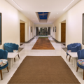Elegant hotel corridor with blue velvet scallop chairs, botanical artwork, herringbone wood floor inlay, and a skylight at a luxury property in Goa