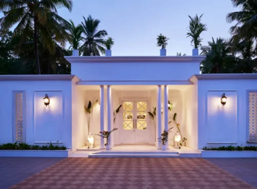 White colonial-style villa entrance in Agonda Beach, Goa, with columned portico, warm lighting, and palm trees at dusk