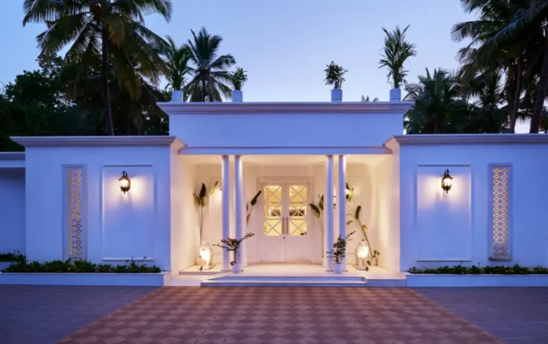White colonial-style villa entrance in Agonda Beach, Goa, with columned portico, warm lighting, and palm trees at dusk