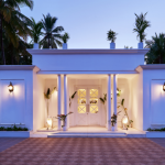 White colonial-style villa entrance in Agonda Beach, Goa, with columned portico, warm lighting, and palm trees at dusk