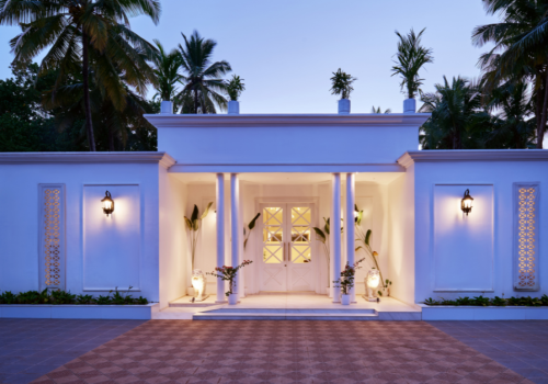 White colonial-style villa entrance in Agonda Beach, Goa, with columned portico, warm lighting, and palm trees at dusk