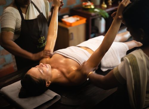 Two therapists performing Ayurvedic postpartum care oil massage on a woman lying on a treatment table