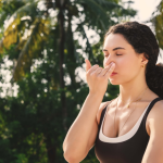 Woman practicing alternate nostril breathing as part of a somatic morning routine surrounded by palm trees