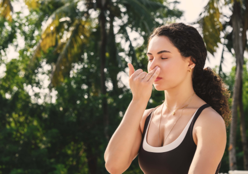Woman practicing alternate nostril breathing as part of a somatic morning routine surrounded by palm trees