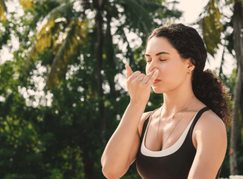 Woman practicing alternate nostril breathing as part of a somatic morning routine surrounded by palm trees