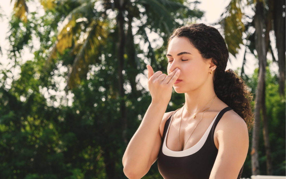 Woman practicing alternate nostril breathing as part of a somatic morning routine surrounded by palm trees