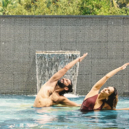 Yoga pose for core strength – man and woman practicing side stretch pose in a resort pool