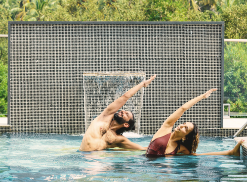 Yoga pose for core strength – man and woman practicing side stretch pose in a resort pool
