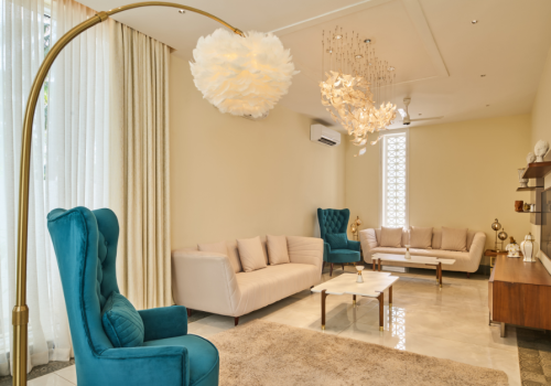 Elegant living room with teal wingback chairs, cream sofas, and a gold arc floor lamp beneath a feather pendant light.