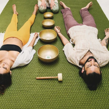 Yoga for chronic stress with two guests resting beside Tibetan singing bowls during a guided relaxation session.