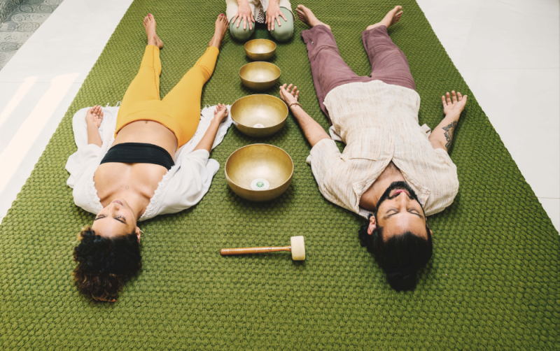 Yoga for chronic stress with two guests resting beside Tibetan singing bowls during a guided relaxation session.