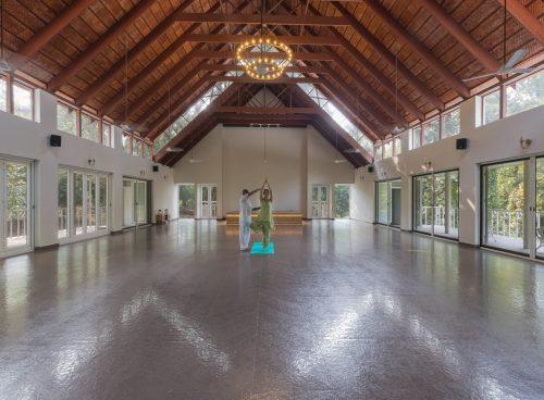 Yoga to lower cortisol: A guided yoga session at Kairali Ayurvedic Healing Village in Palakkad, Kerala, inside a spacious, naturally lit yoga hall.